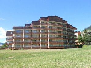 Un immeuble à plusieurs étages doté de balcons, d’un toit plat et d’une pelouse devant.