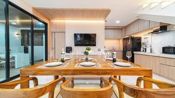 A modern kitchen with wooden cabinetry, a dining table set for four, and a flat-screen TV mounted on the wall.
