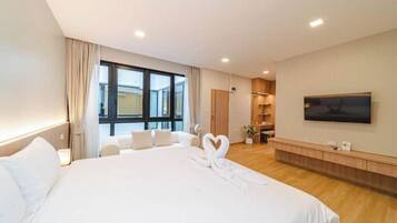 A hotel room with a large bed, a TV mounted on the wall, and a view of the city through the window.