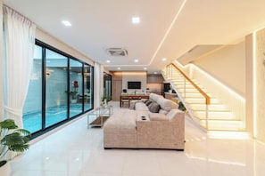 A modern living room with a large sofa, a dining area, and a staircase. - Serene Pool Villa Pattaya 2 (Chonburi)
