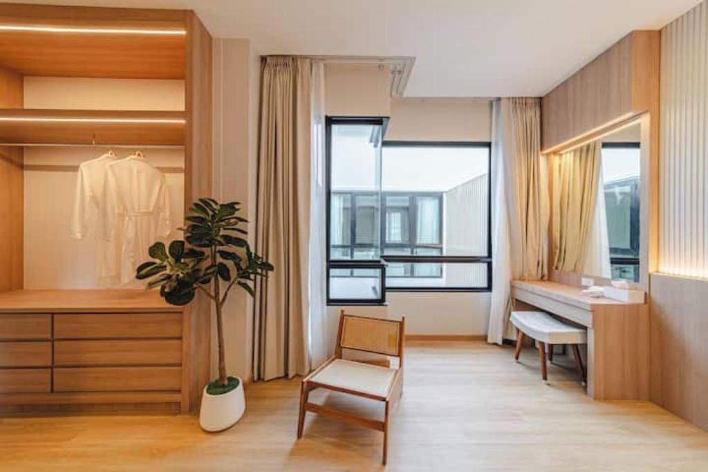 A modern room with a wooden floor, a large window, a chair, a desk, and a plant.