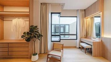 A modern room with a wooden floor, a large window, a chair, a desk, and a plant.