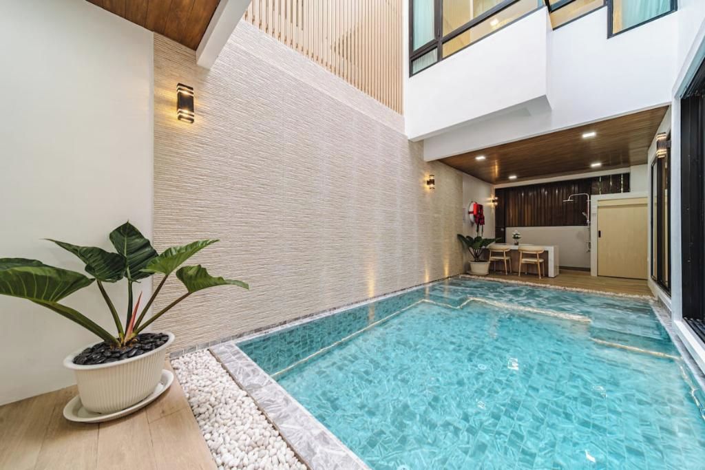 Una piscina interna moderna con superficie d'acqua blu trasparente, circondata da un cordolo di pietre e una pianta in vaso sul lato sinistro.