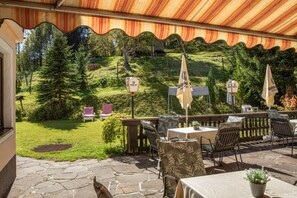 Eine Terrasse im Freien mit Steinboden, Tischen, Stühlen und Sonnenschirmen.
