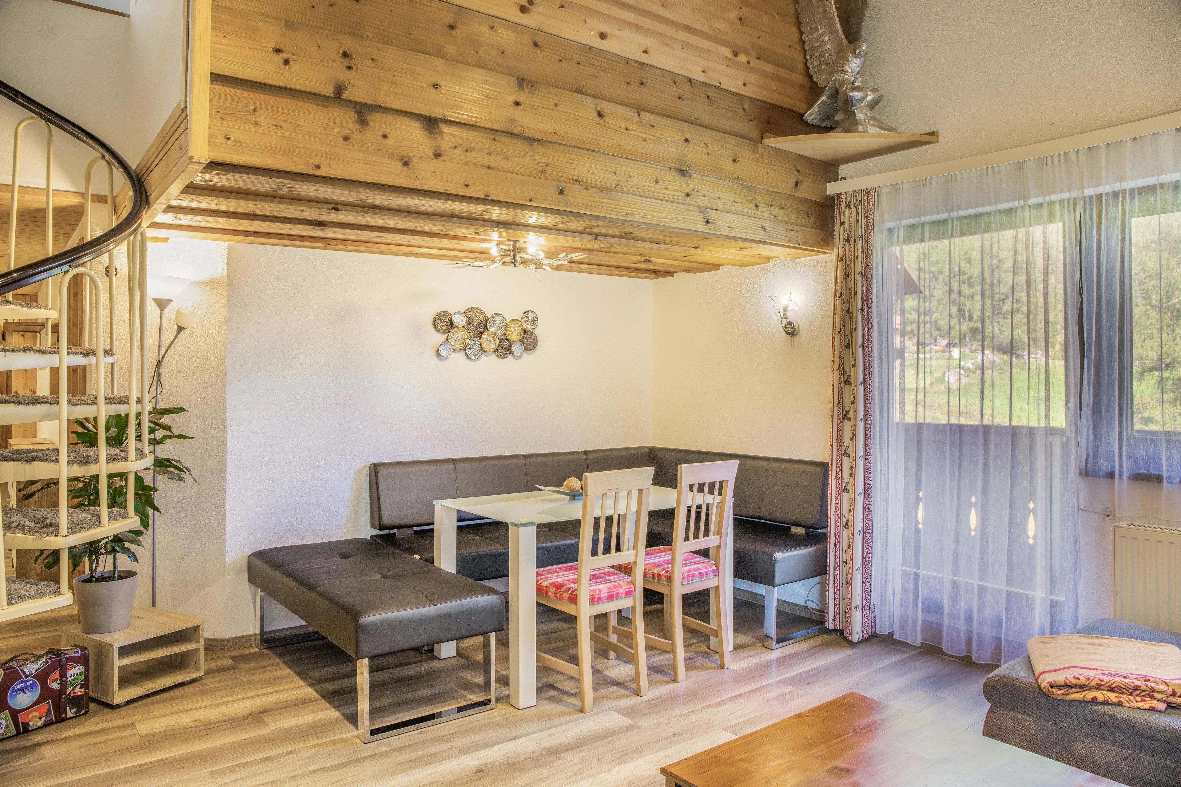 A modern interior with a wooden ceiling, a dining area with a table and chairs, a sofa, and a large window with curtains.