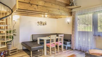 A modern interior with a wooden ceiling, a dining area with a table and chairs, a sofa, and a large window with curtains.