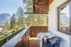 Een balkon met een tafel en stoelen, met uitzicht op een bergachtig landschap met bomen en gebouwen.