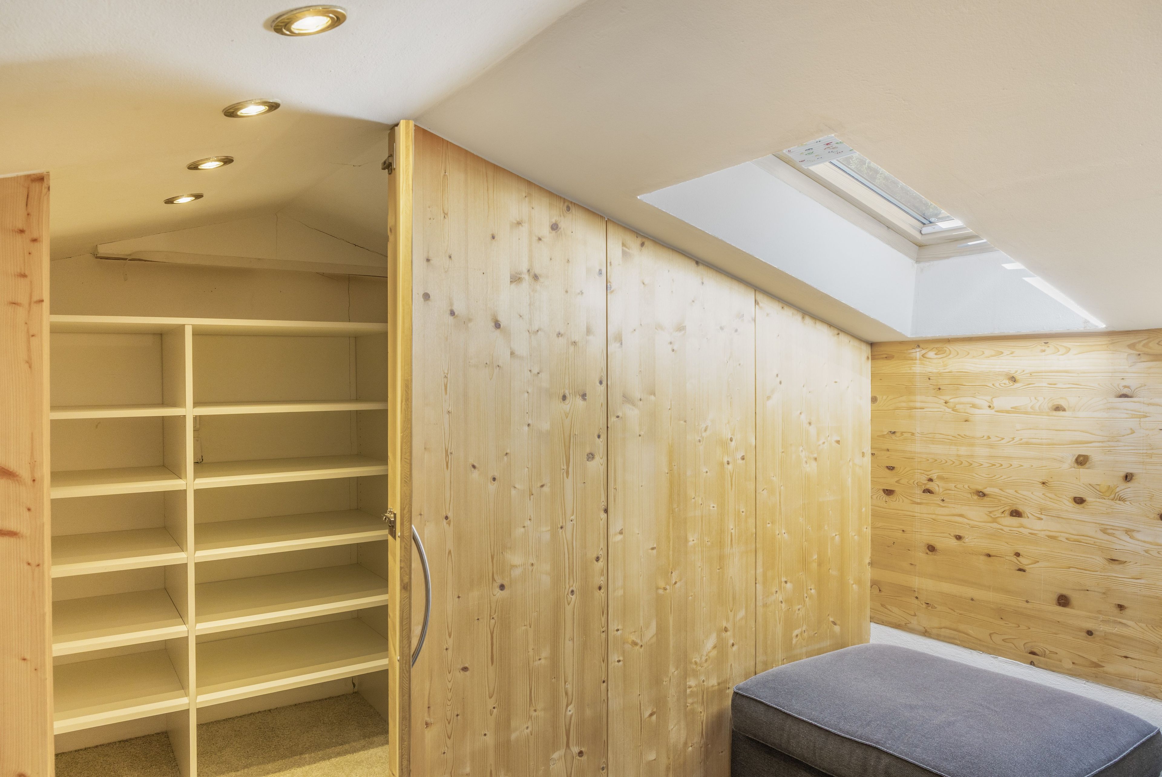 Una habitación con techo inclinado, paredes de madera y una estantería empotrada.
