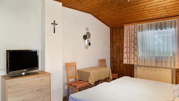 Een slaapkamer met een bed, een tv op een dressoir, een kruis aan de muur en een raam met gordijnen.