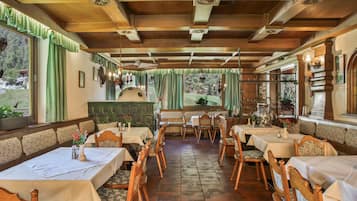 Een restaurant met houten balken, groene gordijnen en uitzicht op het landschap. Tafels zijn gedekt met witte tafelkleden en houten stoelen.