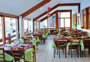 A dining area with multiple tables and chairs, large windows, and wooden beams on the ceiling. - Fitness, swimming pool, hammam, parking, tv, ski locker, 35m², Les Rousses (Prémanon)