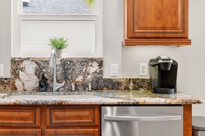 A kitchen with a granite countertop, a stainless steel faucet, a coffee maker, wooden cabinets, and a dishwasher. - Caroline Cove - 3/2 w/ PRIVATE POOL & GOLF CART in The Villages - Caroline. Dog Friendly (Caroline, The Villages)