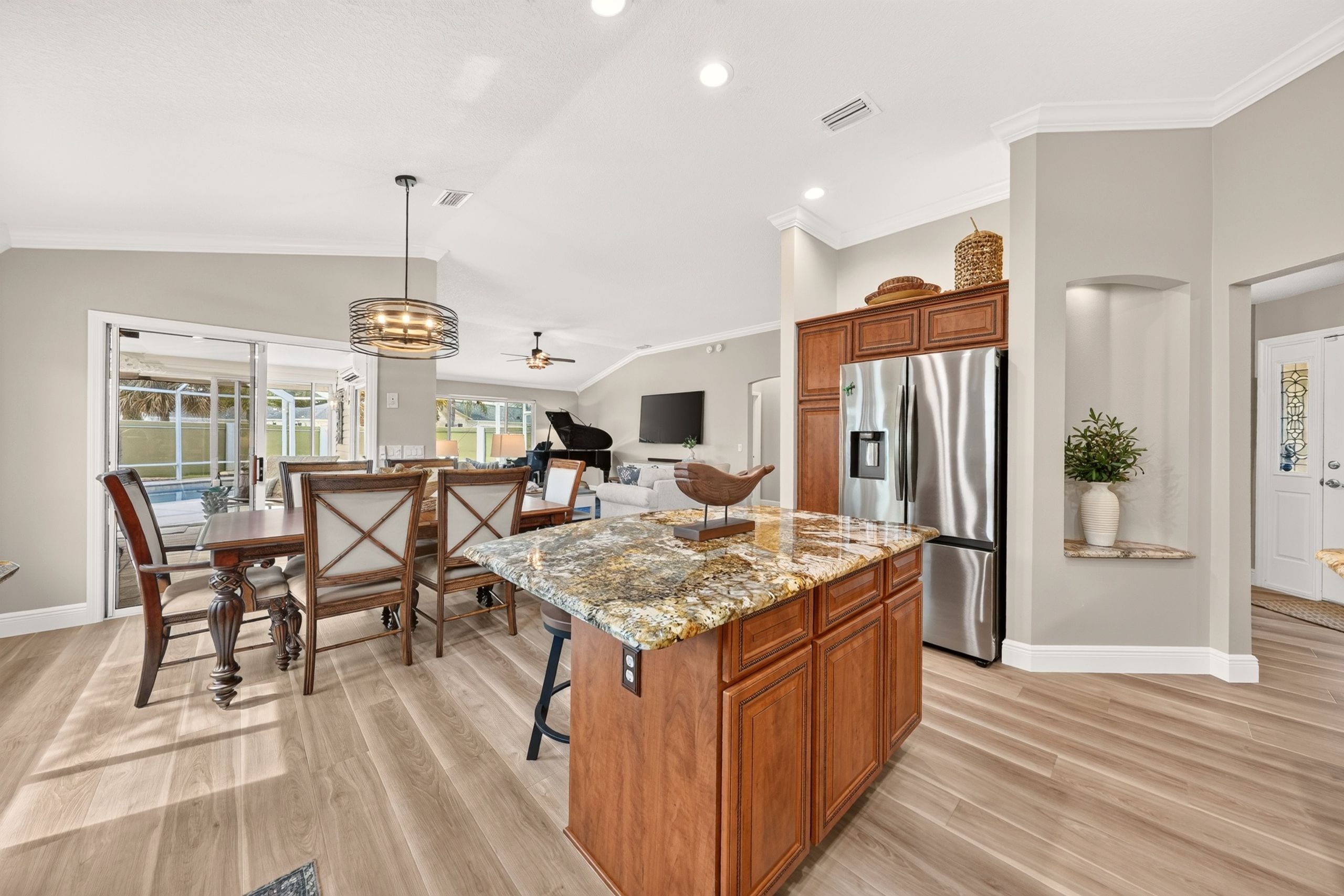 A modern kitchen with a central island, wooden cabinets, and a stainless steel refrigerator.