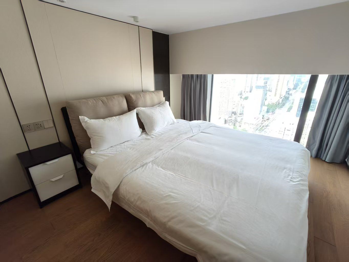 A modern hotel room with a large bed, a nightstand, a wardrobe, and a window with curtains.