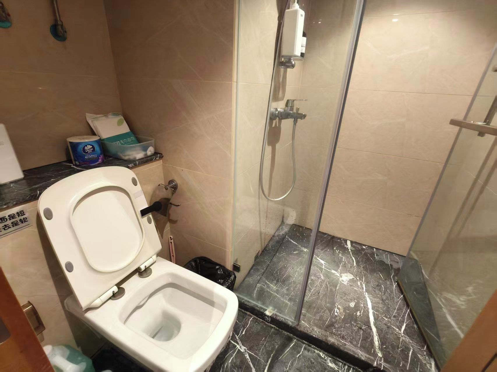 Un baño con inodoro, ducha y suelo de mármol.