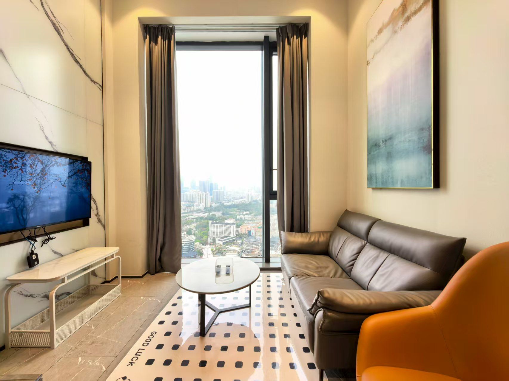 Una sala de estar moderna con sofá, mesa de centro, televisor y vista panorámica de un paisaje urbano a través de un ventanal.