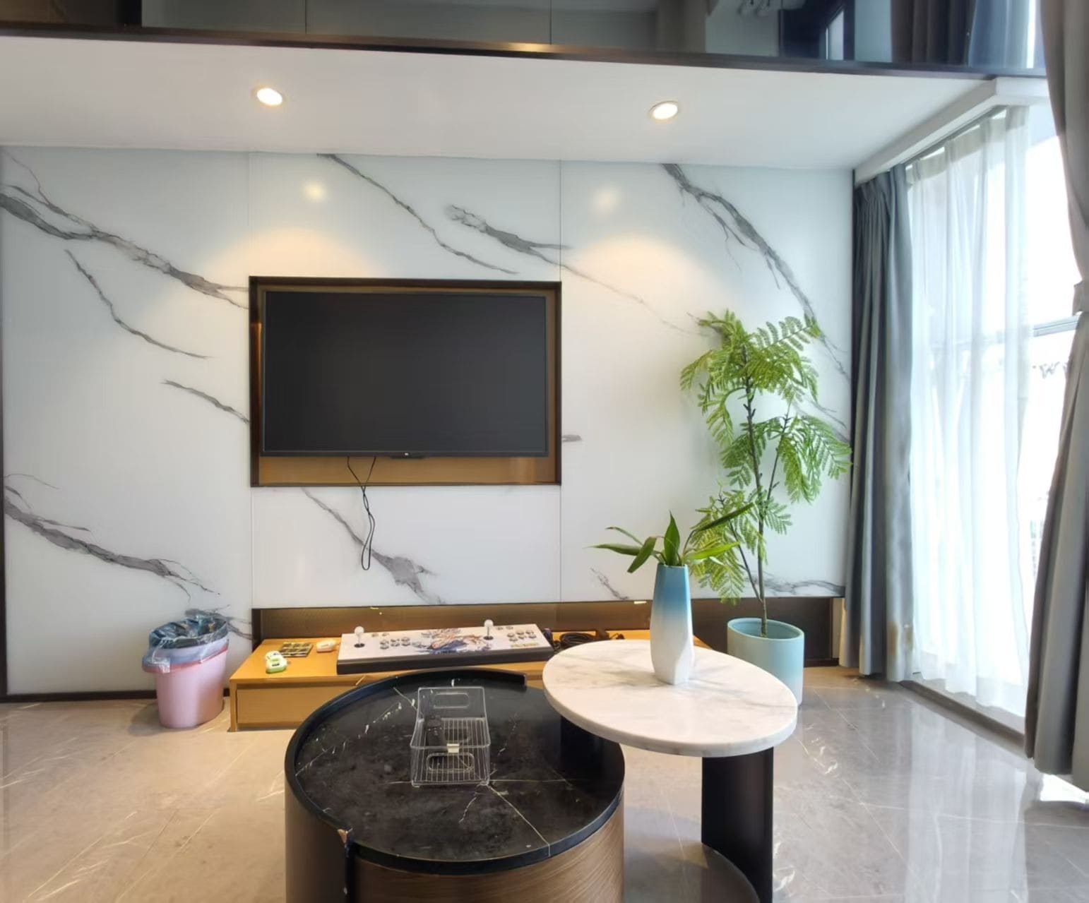 Una sala de estar moderna con un televisor de pantalla plana montado en la pared, una mesa redonda de centro, una planta en maceta y un sofá.