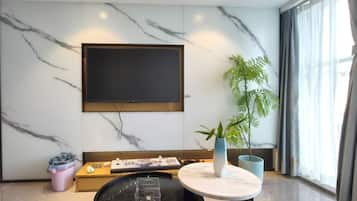 Una sala de estar moderna con un televisor de pantalla plana montado en la pared, una mesa redonda de centro, una planta en maceta y un sofá.