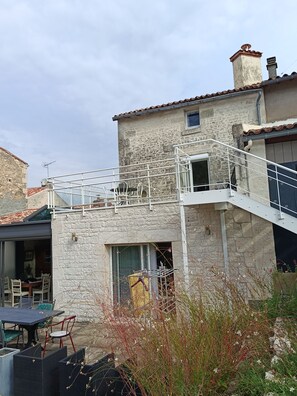 Un bâtiment en pierre doté d’un balcon, d’un espace extérieur aménagé pour s’asseoir et d’un escalier.
