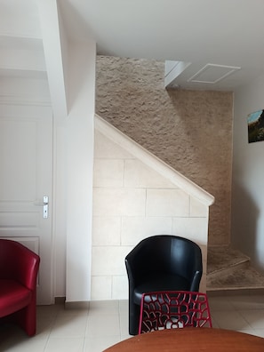 Une pièce avec une porte blanche, un escalier aux murs de couleur beige, une chaise rouge, une chaise noire et une table en bois.