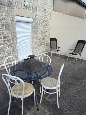 An outdoor patio with a round metal table, white chairs, and a black grill. - In the heart of town, duplex with parking and secure bike storage. (Fontenay-le-Comte)