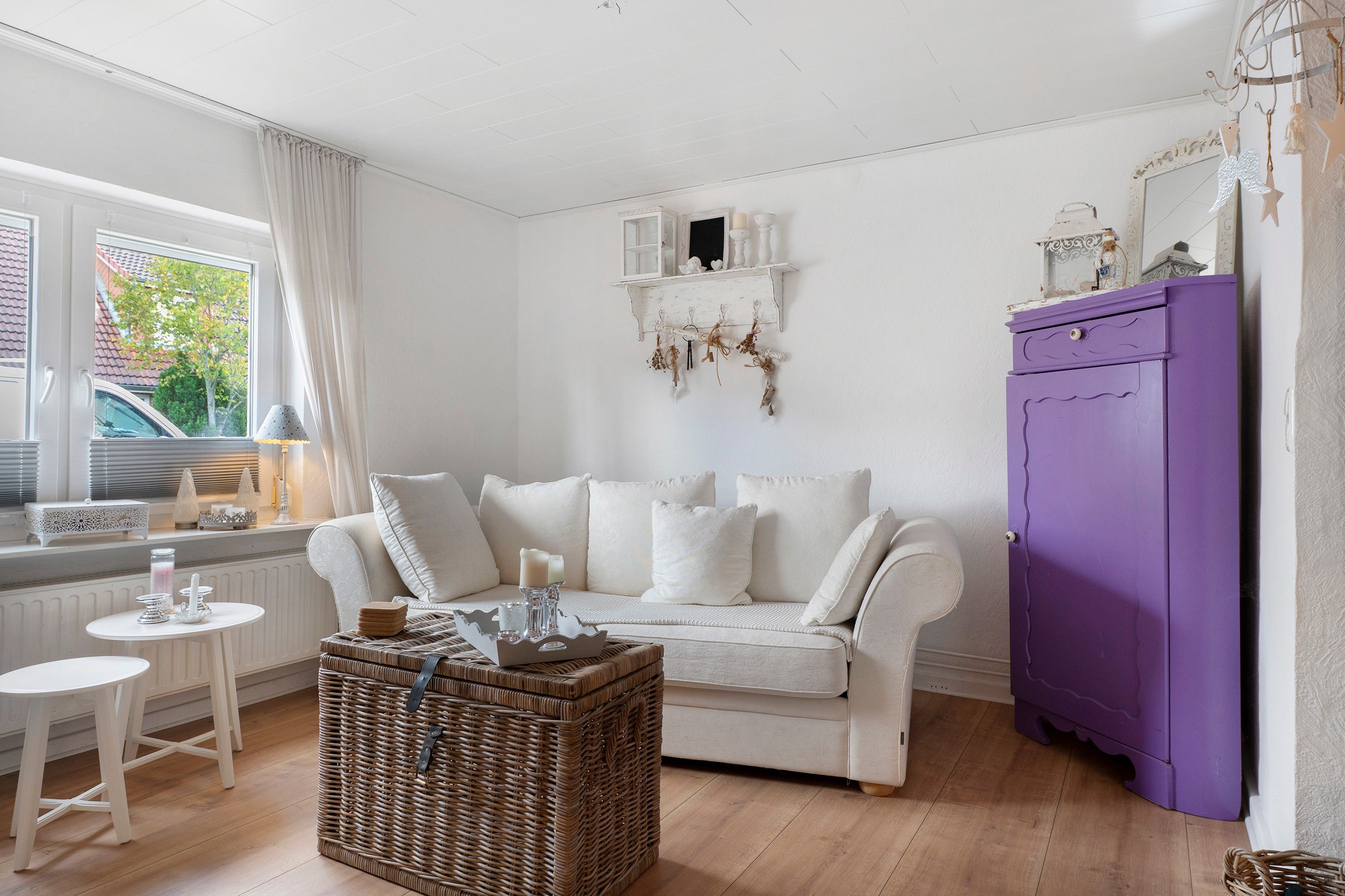 Un salon chaleureux avec un canapé blanc, un meuble violet et une table basse en osier.