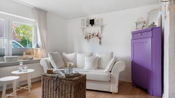 Un salon chaleureux avec un canapé blanc, un meuble violet et une table basse en osier.