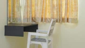 Una habitación con escritorio, silla y ventana con cortinas.