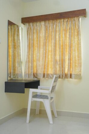 Quarto com escrivaninha, cadeira e janela com cortinas.