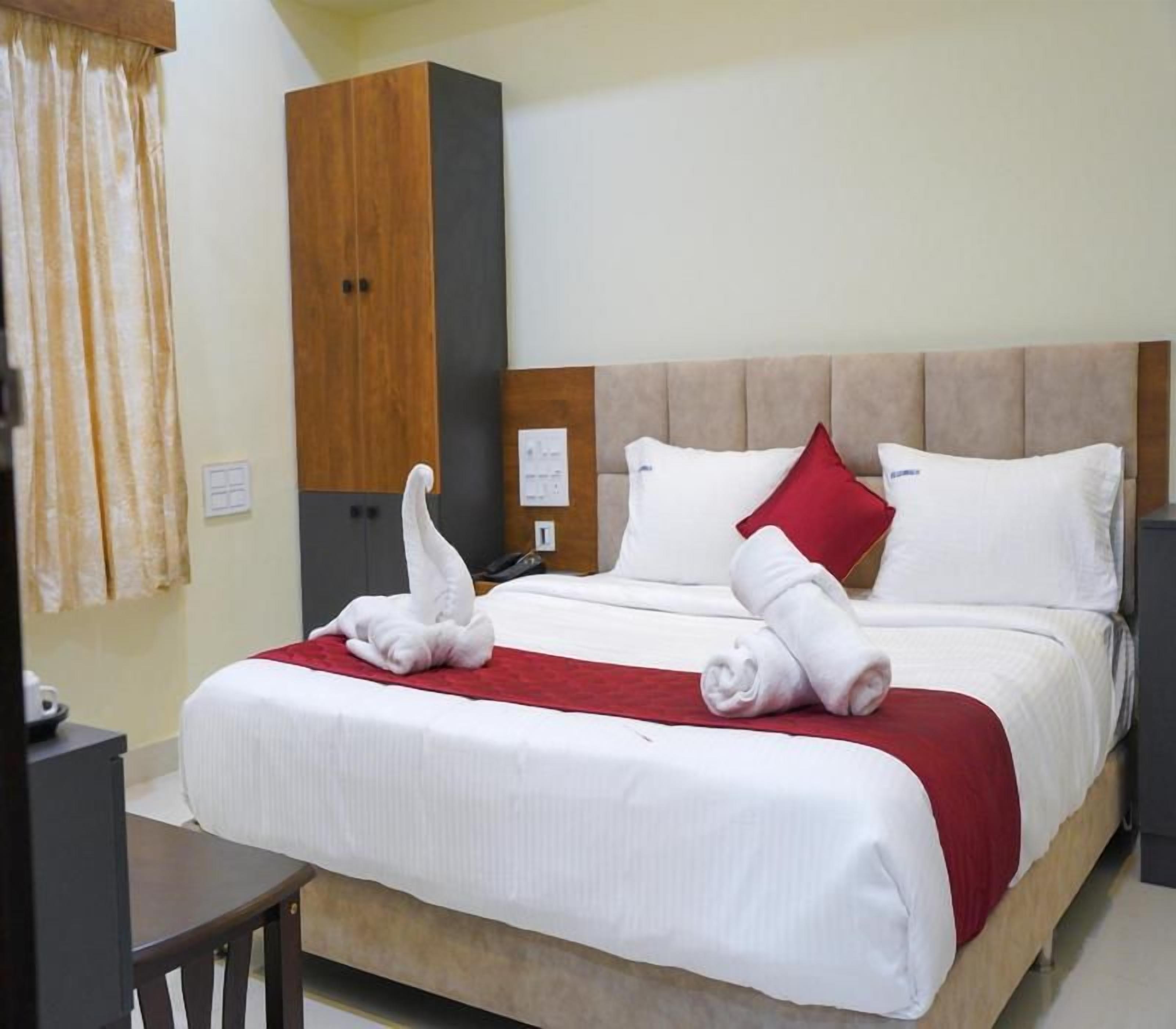 Una camera d'albergo con un letto, un armadio in legno, una scrivania e una coperta rossa.