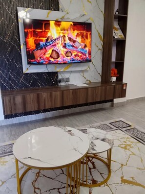 Una sala de estar moderna con un televisor de pantalla plana montado en una pared de mármol, un mueble de madera debajo y un suelo con diseño de mármol.