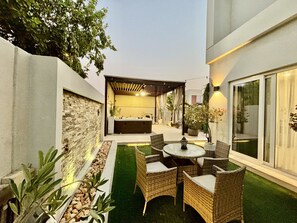 A modern outdoor patio with a round table and wicker chairs, a built-in hot tub, and a stone wall. - Villanova Amaranta 3 -298 3BD (Dubai)