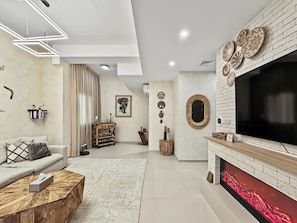 A modern living room with a fireplace, a large TV, and a sofa. - Villanova Amaranta 3 -298 3BD (Dubai)