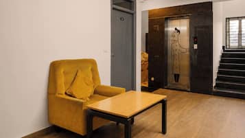 Una habitación con un sillón amarillo, una mesa de madera, una puerta gris y una escalera con ascensor.