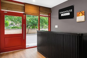 Ein Empfangsbereich mit roter Tür, einem schwarzen Empfangstresen und einem Schild, das 'Townhouse' und 'Vollständig Servisiert' anzeigt.