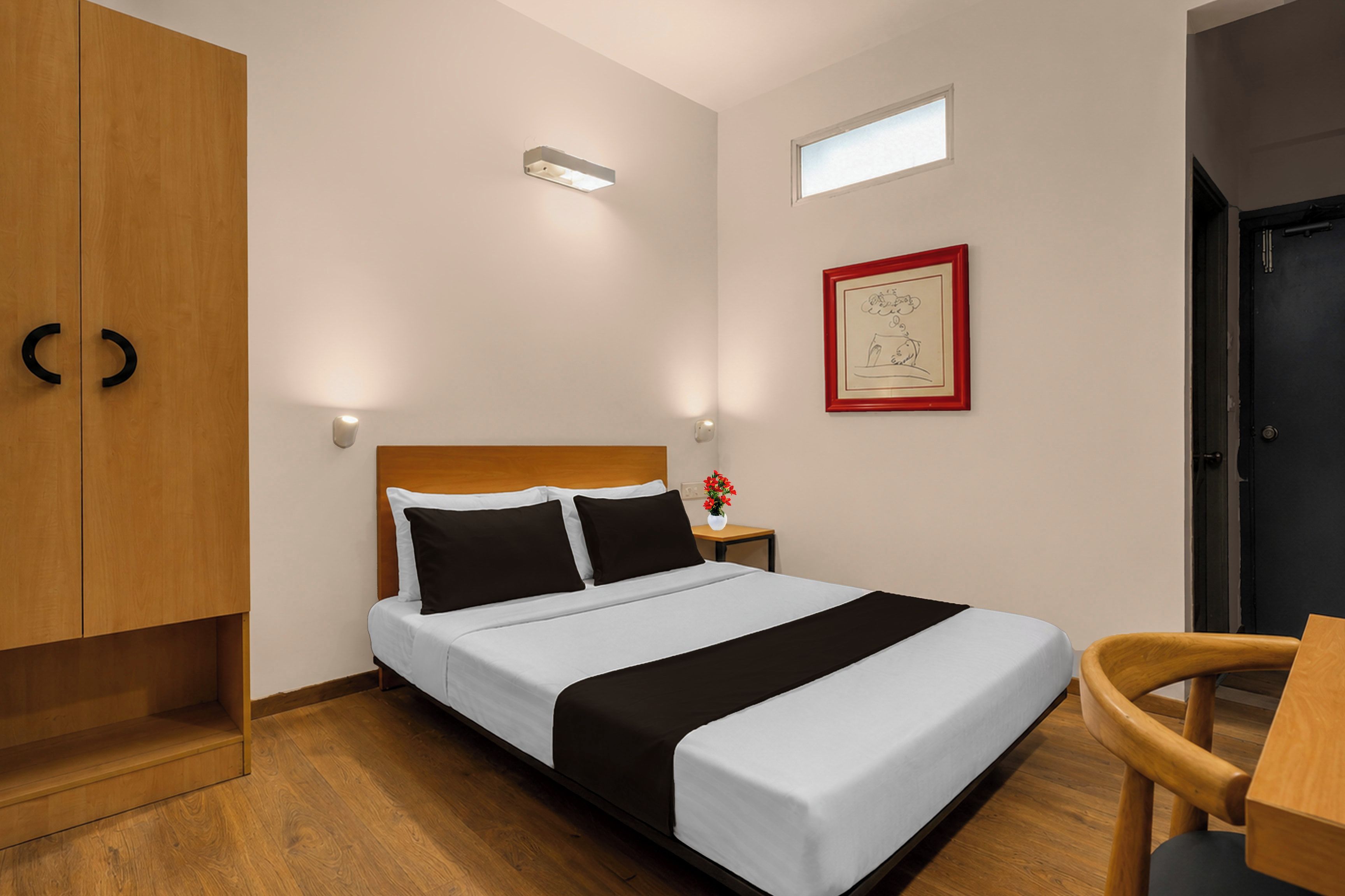 Habitación de hotel con cama, armario de madera, mesita de noche y una ventana pequeña.