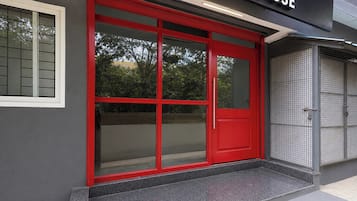 Una puerta roja con un panel de vidrio, un portón de metal y un edificio con fachada gris.