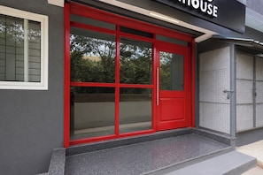 Una puerta roja con un panel de vidrio, un portón de metal y un edificio con fachada gris.