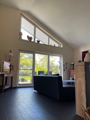 A spacious living room with a large window, a sofa, a television, and a wooden cabinet. - Pet-friendly vacation home just 10 minutes away from Safari Park & Bird Park (Böhme)