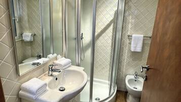 Ein modernes Badezimmer mit einer gläsernen Dusche, einem Waschbecken, einem Bidet und einem Schminktisch mit Pflegeprodukten.