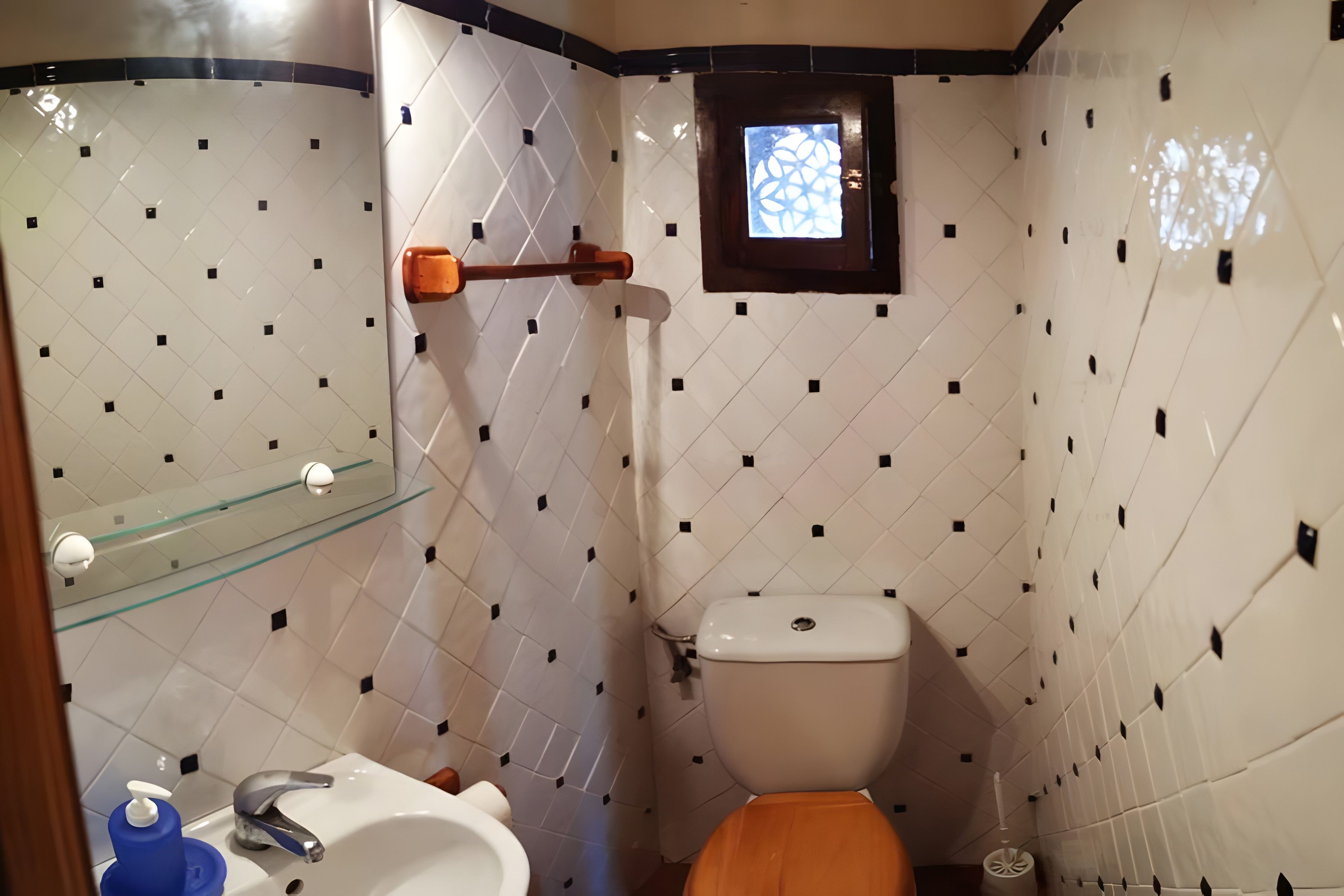 Une salle de bain avec des toilettes, une étagère en verre, un distributeur de savon liquide et une fenêtre.