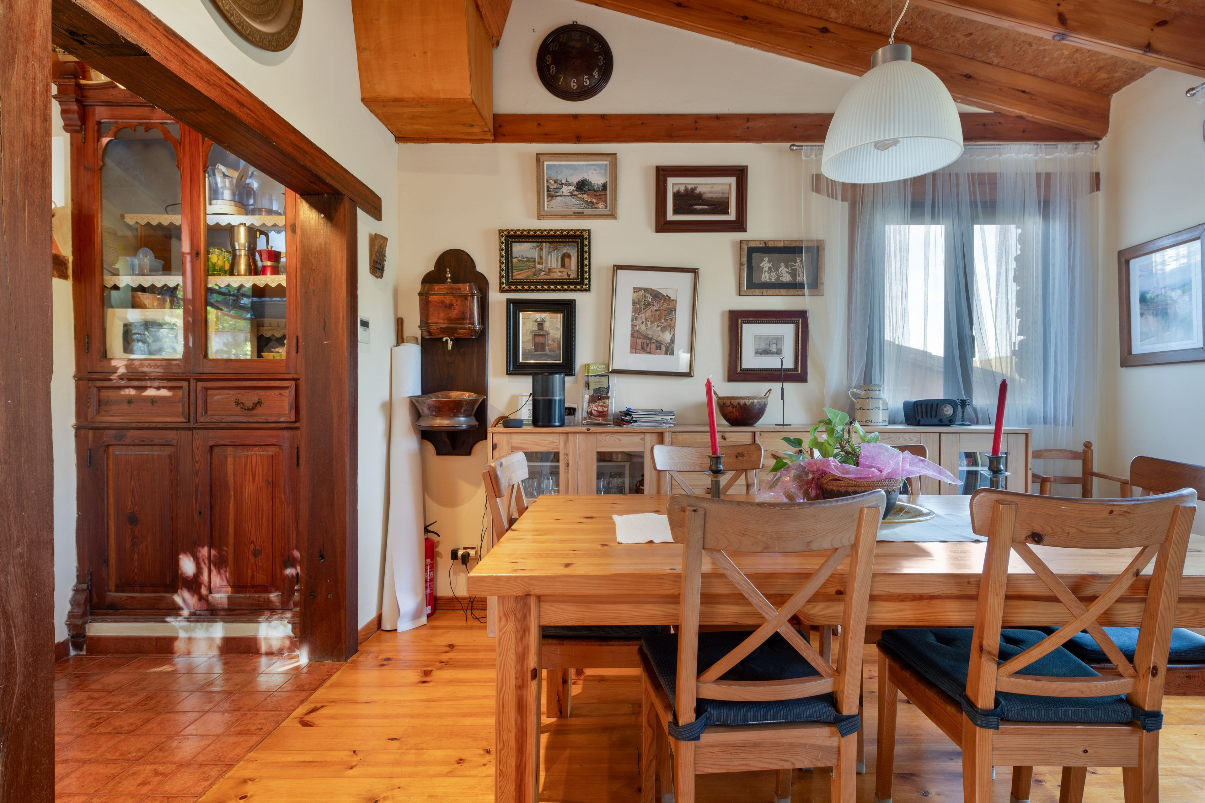 A wooden dining table with chairs, a kitchen area with wooden cabinets, and various framed pictures on the wall.