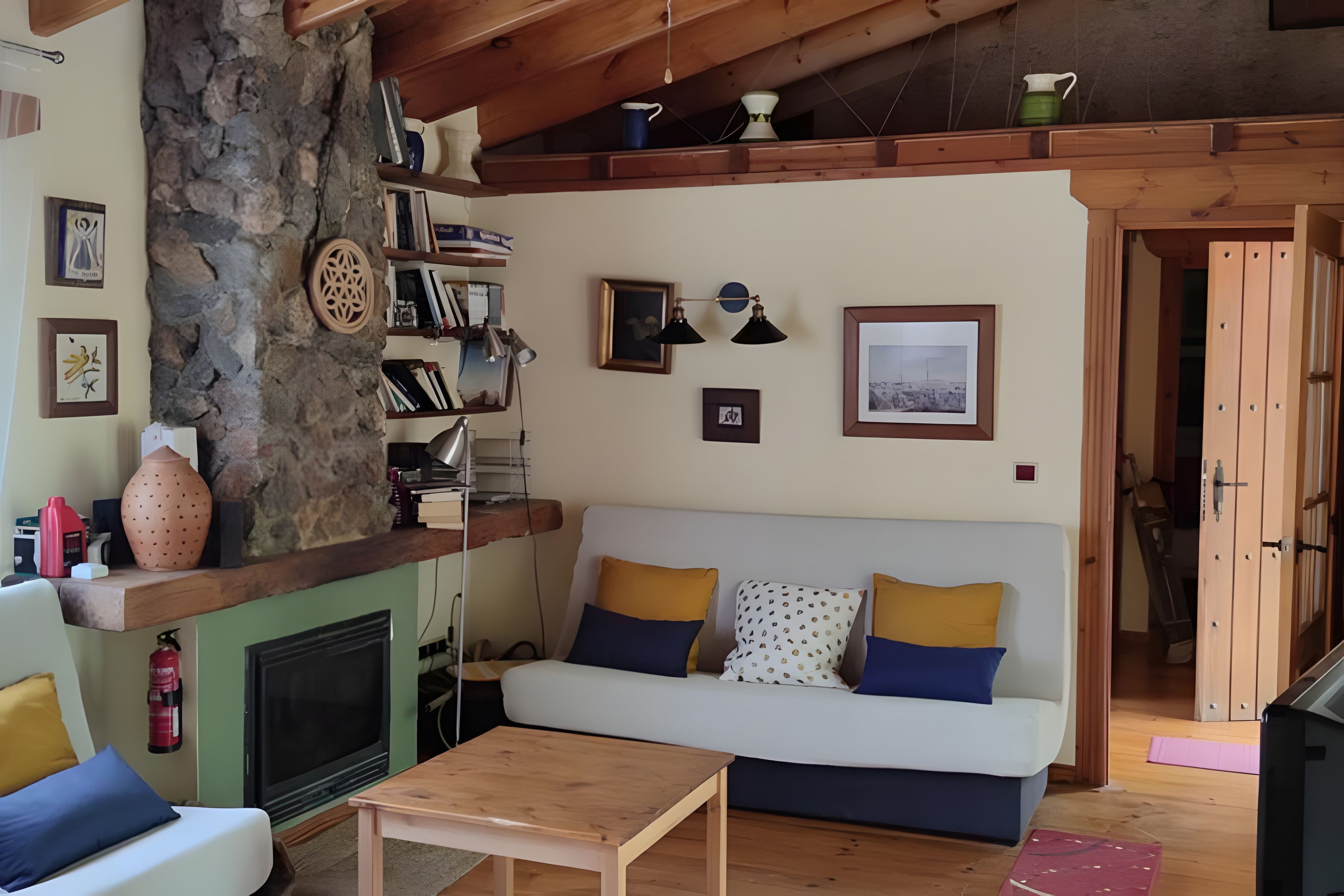 Una sala de estar acogedora con una pared de piedra, una chimenea, un sofá con cojines y una mesa de centro de madera.