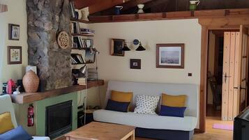 Una sala de estar acogedora con una pared de piedra, una chimenea, un sofá con cojines y una mesa de centro de madera.