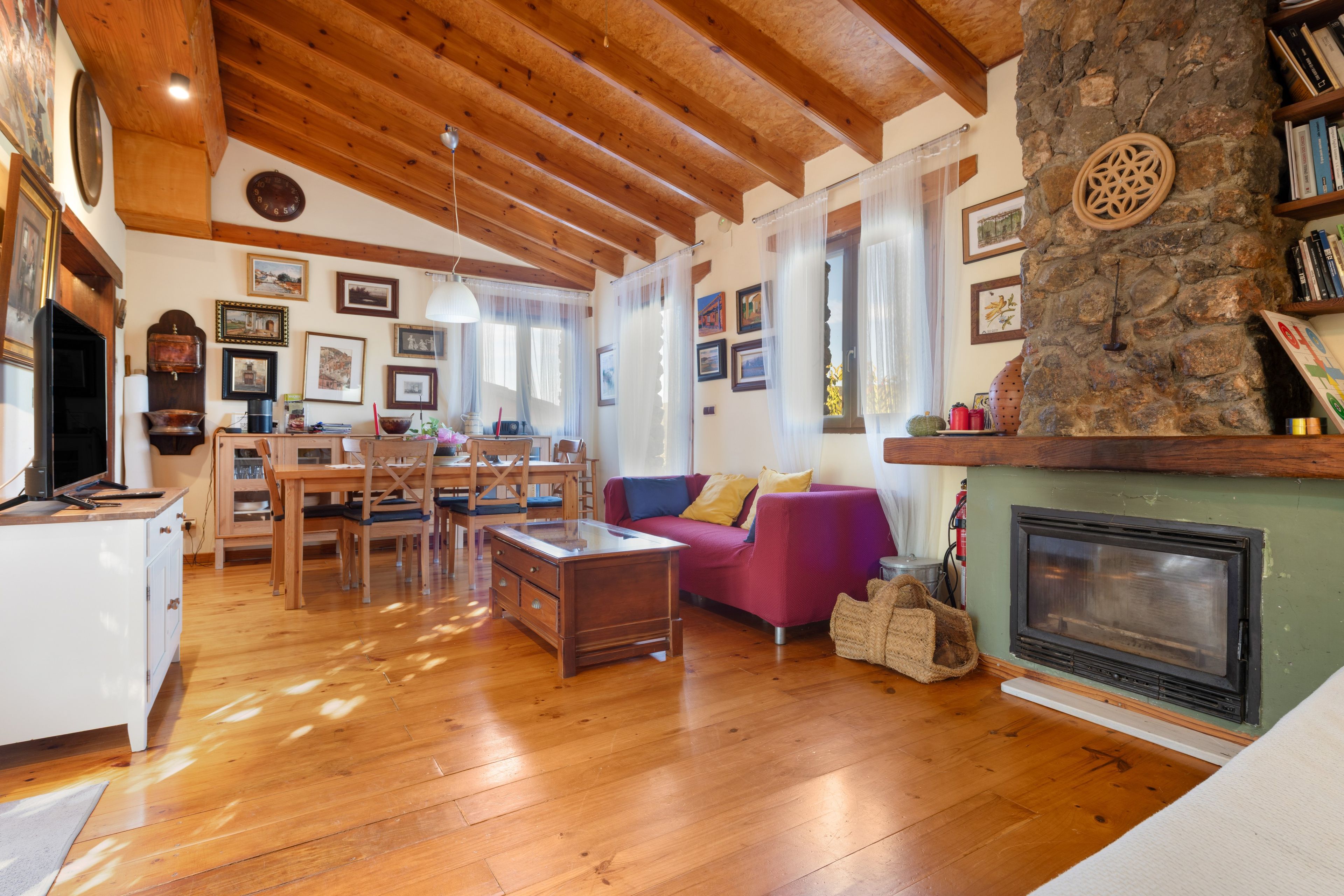 Una sala de estar acogedora con pisos de madera, una chimenea de piedra y un comedor con una mesa y sillas de madera.