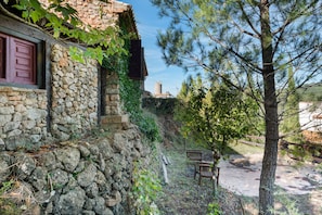 A stone building with a red door, a bench, and a tree in a courtyard.