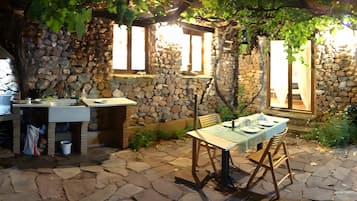 An outdoor dining area with stone walls, a table set for two, and a stone floor.