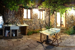 Un área de comedor al aire libre con paredes de piedra, una mesa lista para dos personas y piso de piedra.