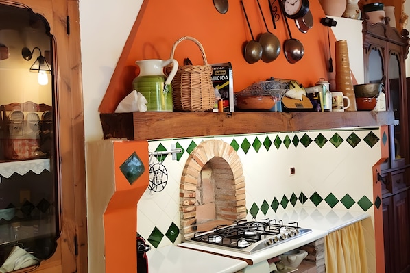 Una cocina con estufa a gas, horno de ladrillo y diferentes utensilios y recipientes en la encimera.
