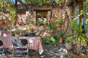A stone building with a checkered table and chairs outside, surrounded by potted plants and a stone wall.